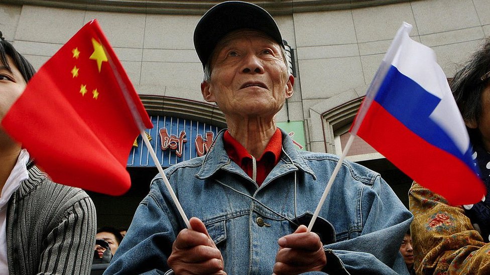 A man holding both Russian and Chinese flags