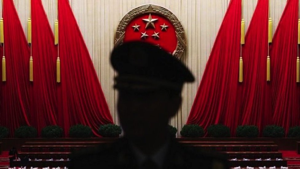 The silhouette of a man in uniform in front of large red flags in a hall