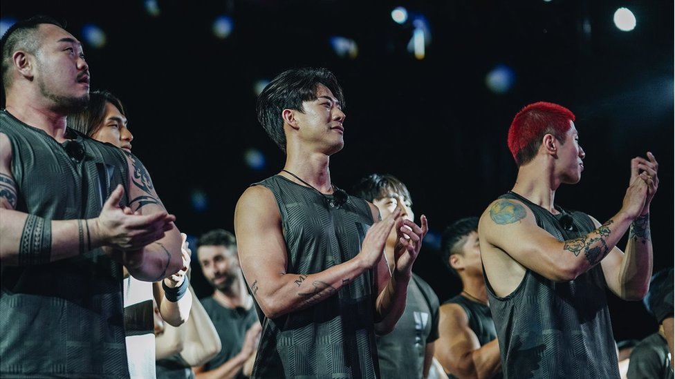 Contestants clapping, some with tattoos